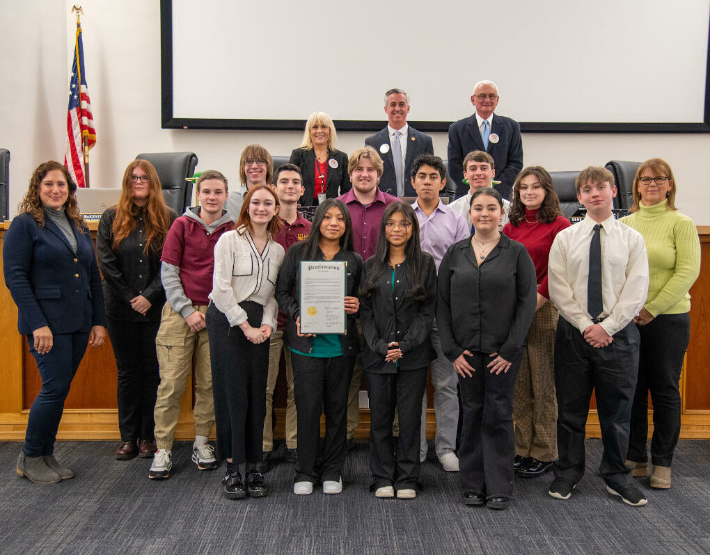 Smiling students in a group with county commissioners in suits standing above and behind them