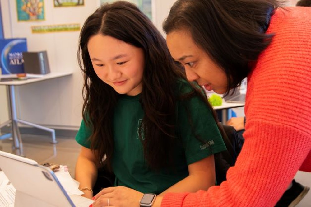 A student and adult mentor working at a desk.